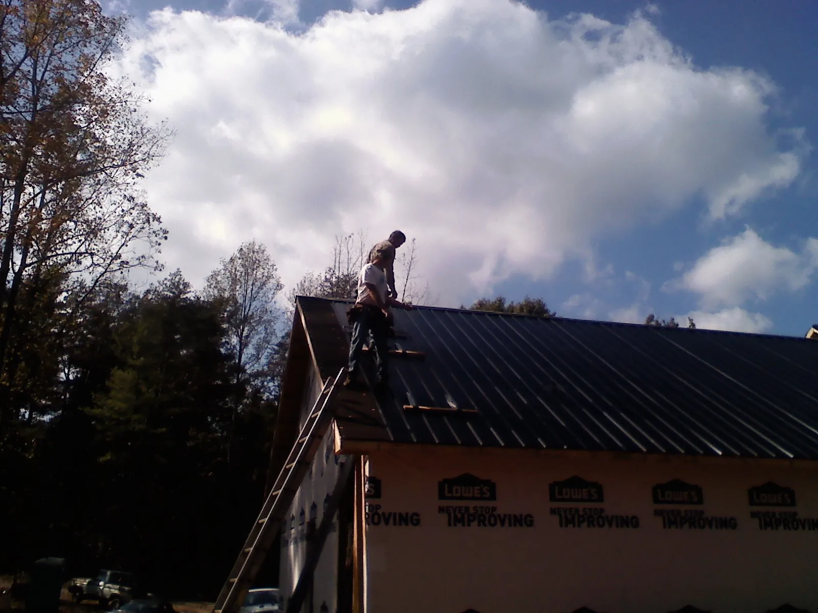 Roofer fastening dark metal panels high against a cloudy sky in Midvale